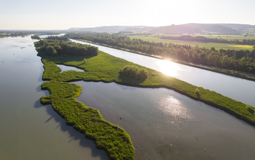 Luftbild einer renaturierten Flusslandschaft im Sonnenuntergang mit reichlich Grünflächen und Gewässern, die als Lebensraum für einheimische Tierarten dienen, ähnlich den geplanten Renaturierungsprojekten beim Kraftwerk Gratkorn.